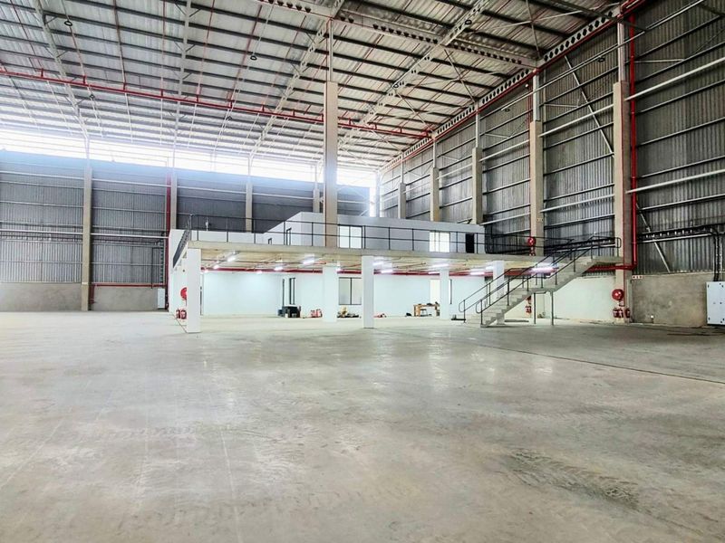 Spacious industrial warehouse featuring a mezzanine level, steel staircase, high-clearance roof structure, and concrete flooring, suitable for various commercial or storage operations.