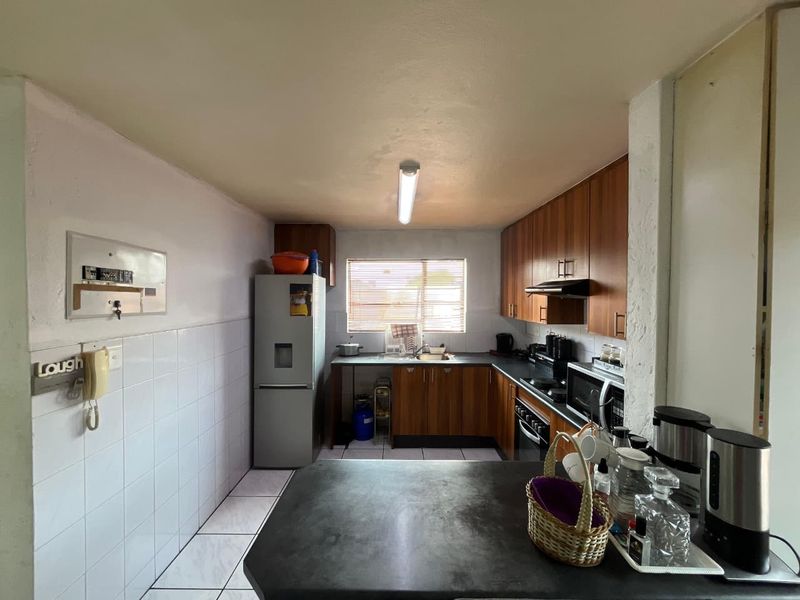 A functional kitchen featuring wood-finish cabinetry, tiled splashbacks, and a breakfast counter, offering a practical layout with integrated appliances.