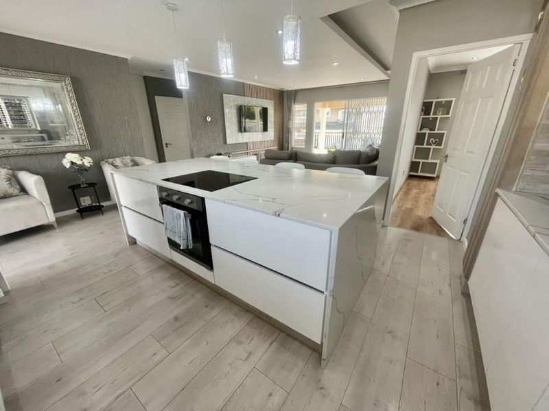 Modern open-plan living area featuring a sleek kitchen island with integrated oven and hob, complemented by contemporary lighting and light-toned laminate flooring.