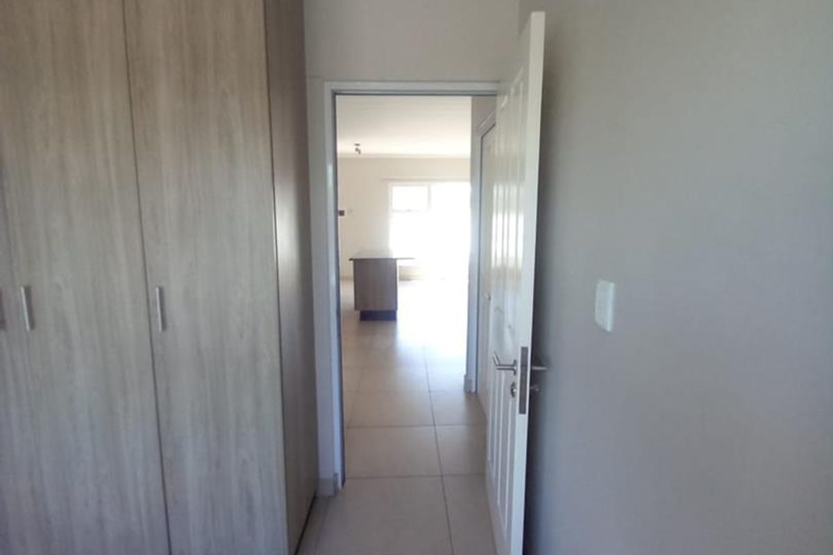 A view from a bedroom featuring built-in wooden cupboards, tiled flooring, and a doorway leading to an open-plan living area.