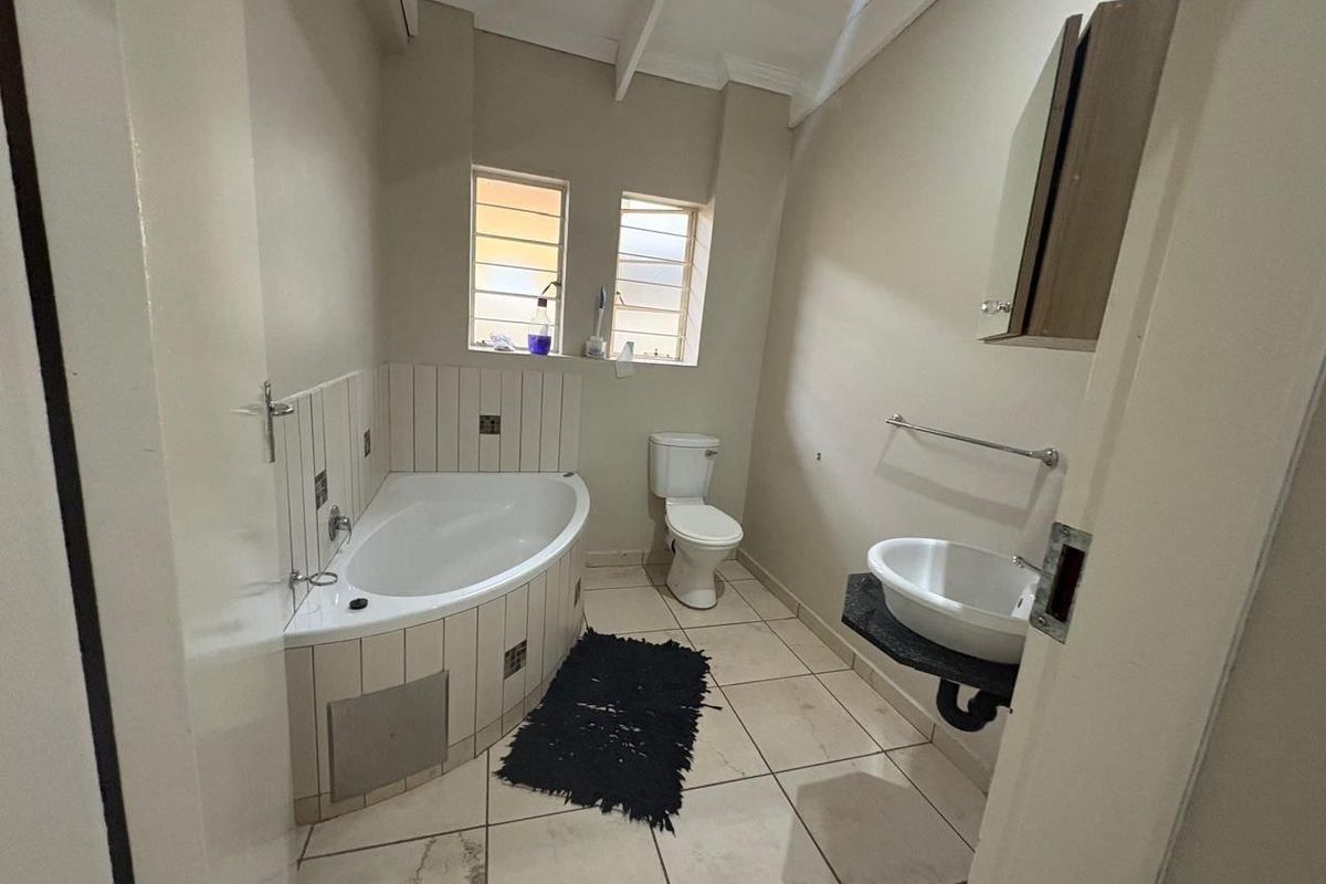 A functional bathroom featuring a corner bathtub, wall-mounted basin, and toilet with tiled flooring and neutral wall finishes.