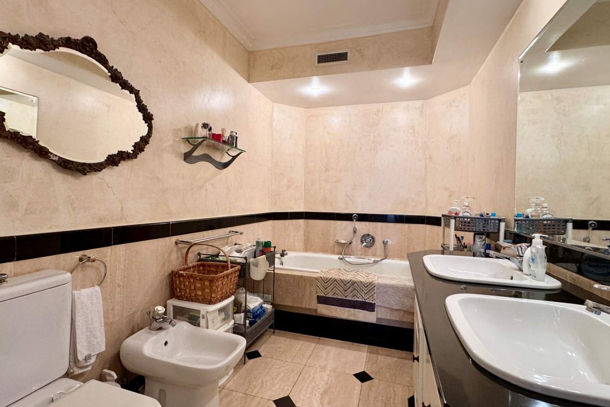 Spacious bathroom featuring a dual vanity, built-in bathtub, bidet, and toilet, finished with elegant stone wall and floor tiling.