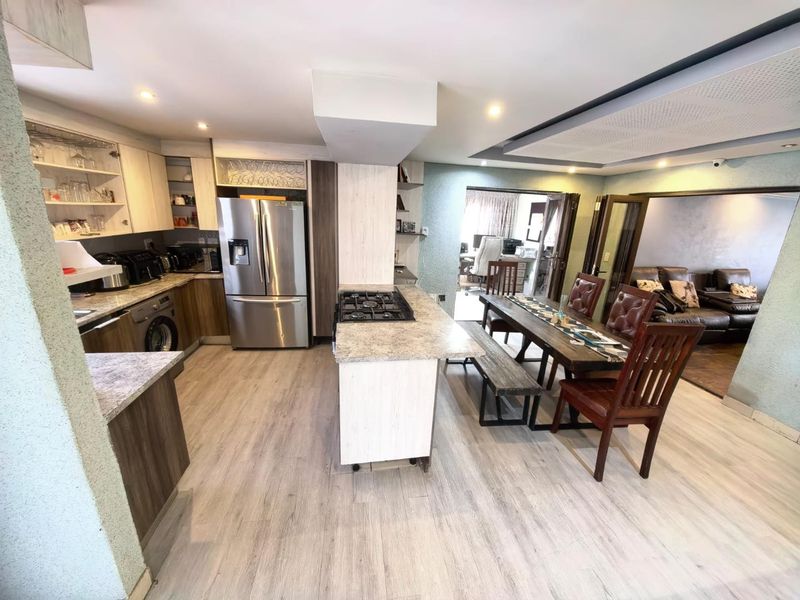 Open-plan kitchen and dining area featuring a central island with gas hob, modern cabinetry, and light wood-look flooring, flowing into adjacent living spaces.
