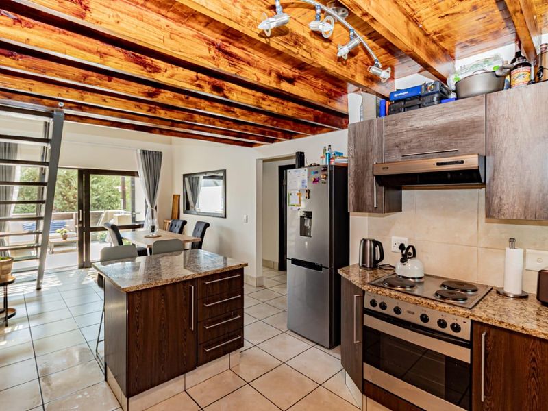 Open-plan kitchen and living area featuring exposed timber ceiling beams, granite countertops, built-in appliances, and direct access to an outdoor patio area.