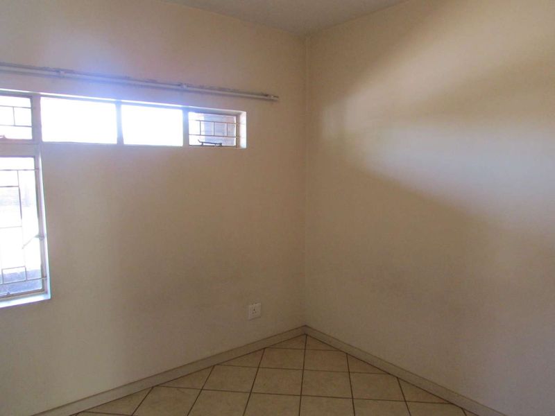 An empty bedroom featuring tiled flooring and metal-framed windows with security bars, requiring minor cosmetic updates to the wall finishes.