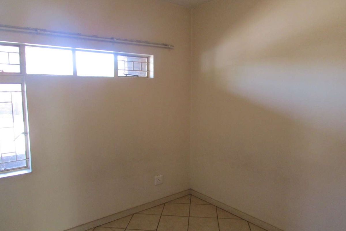An empty bedroom featuring tiled flooring and metal-framed windows with security bars, requiring minor cosmetic updates to the wall finishes.