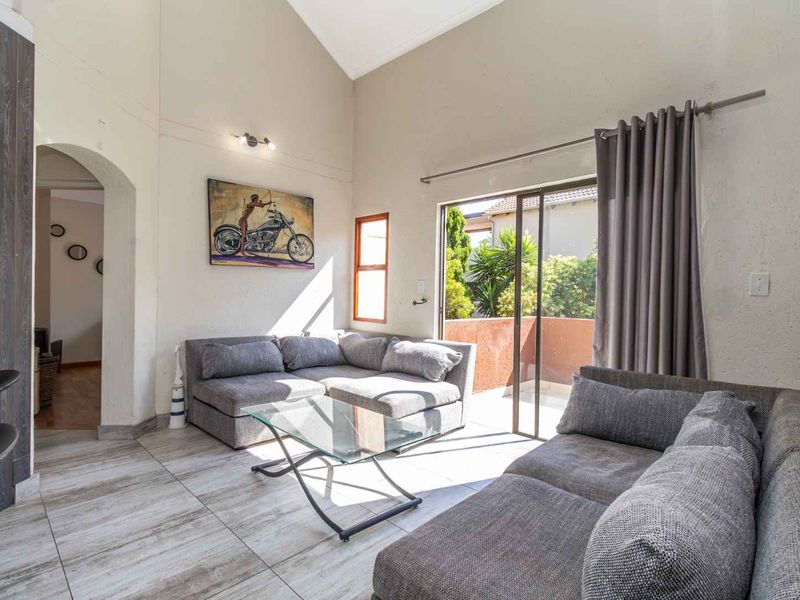 Spacious living room featuring a high vaulted ceiling, tiled flooring, and a sliding glass door providing access to an outdoor balcony area.