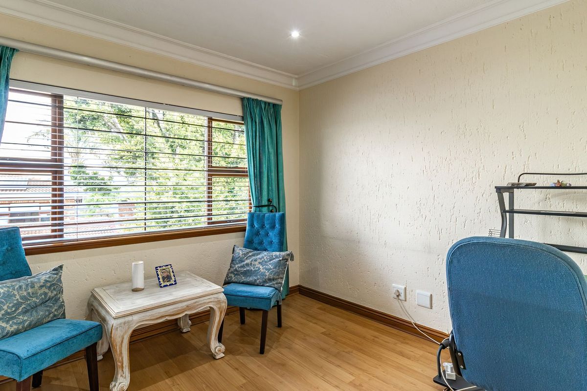 A bedroom featuring laminate flooring, coved ceilings with recessed lighting, and a large window with horizontal blinds.