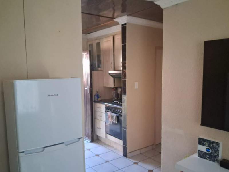 A compact kitchen featuring built-in cabinetry, a fitted oven and hob, and tiled flooring, viewed from an adjacent living area.