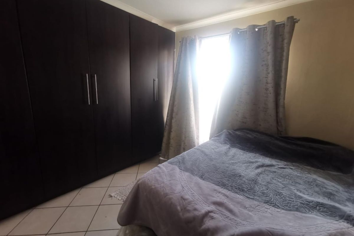 A bedroom featuring dark built-in cupboards and tiled flooring, with natural light entering through the window.