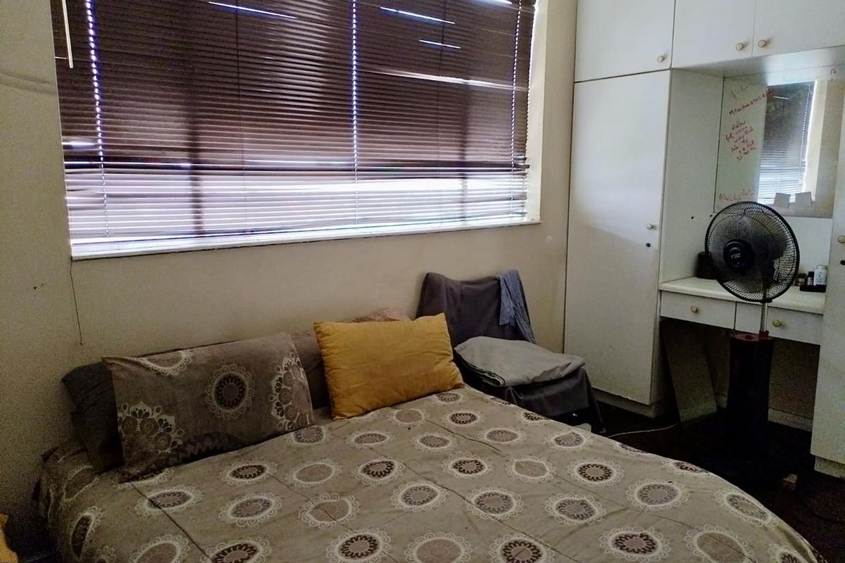 A bedroom featuring built-in white cabinetry and a vanity area, with large windows covered by horizontal blinds.