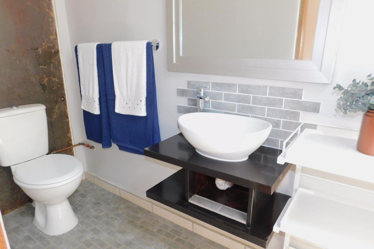 A compact bathroom featuring a modern vessel sink on a floating vanity, tiled backsplash, and a standard toilet with visible wall finish repairs needed.