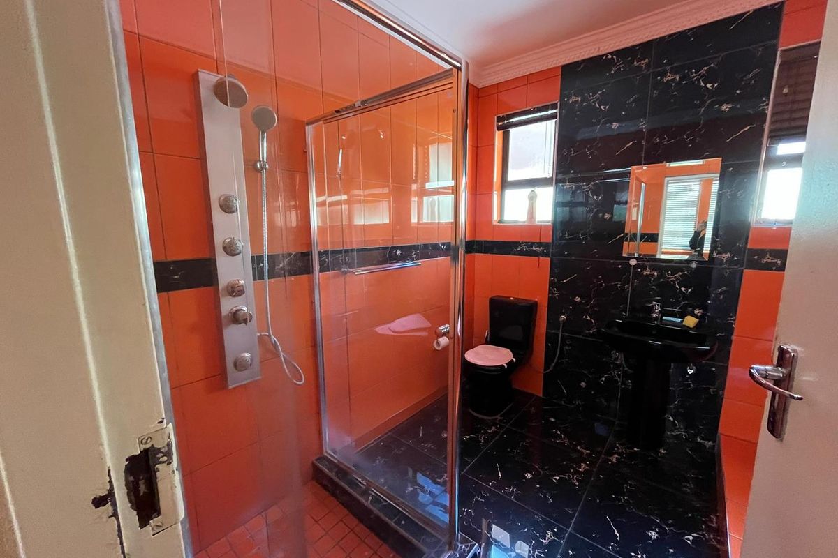 A bathroom featuring a glass-enclosed shower with a wall-mounted shower panel, a black pedestal basin, and a matching black toilet.