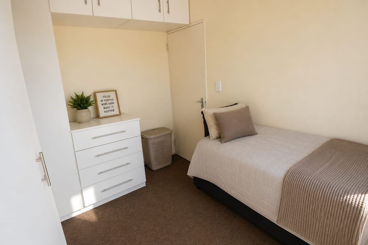 A compact bedroom featuring built-in overhead cupboards and neutral carpeting, providing a functional and tidy living space.