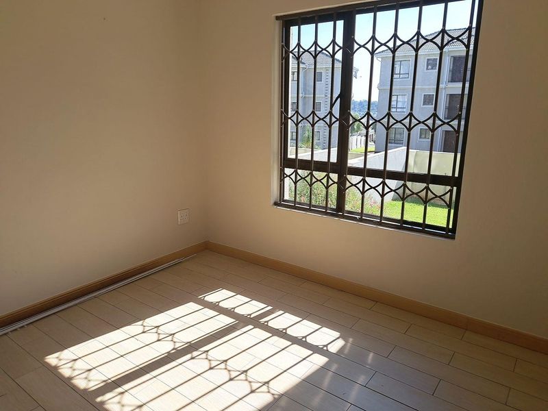 A bright, empty bedroom featuring light-toned laminate flooring and a window fitted with a security gate.