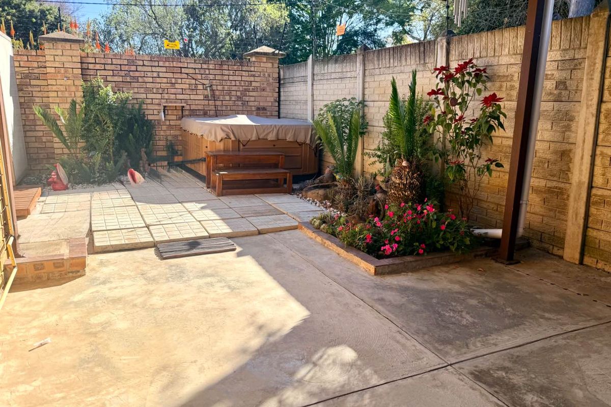 A private rear courtyard featuring a covered patio area, paved flooring, and a built-in brick boundary wall with established garden beds.