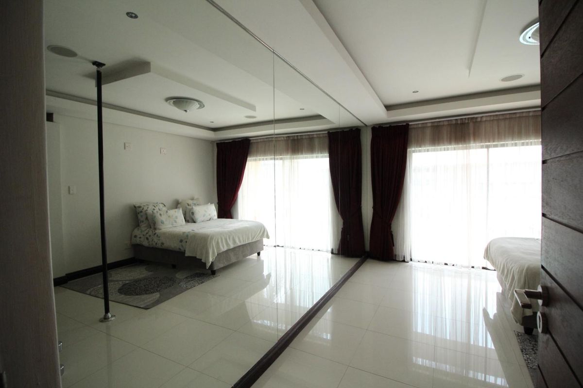 Spacious bedroom featuring large floor-to-ceiling mirrored wall, recessed ceiling lighting, and sliding glass doors providing ample natural light.