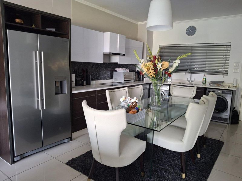 Modern open-plan kitchen and dining area featuring sleek cabinetry, stone countertops, mosaic backsplash, and integrated appliances, creating a functional and contemporary living space.