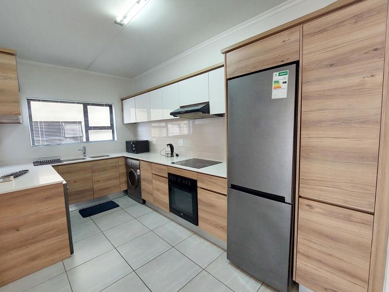 Modern kitchen featuring wood-grain cabinetry, white stone countertops, integrated appliances, and sleek tiled flooring in a clean, well-maintained space.