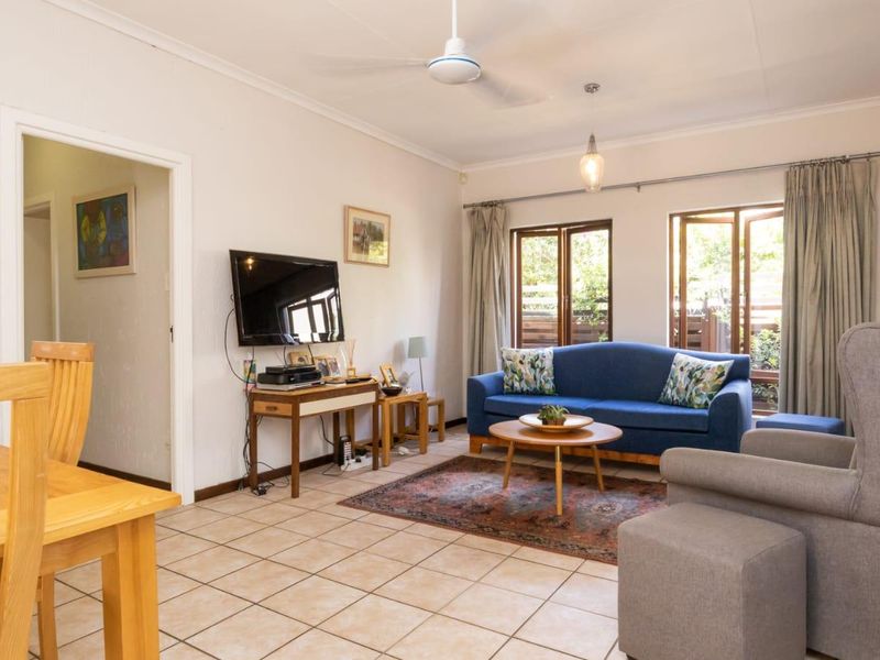 A bright living room featuring tiled flooring, a ceiling fan, and large windows providing natural light and access to the outdoor area.