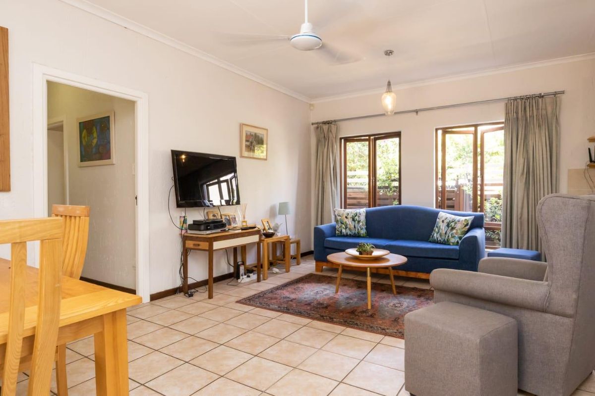 A bright living room featuring tiled flooring, a ceiling fan, and large windows providing natural light and access to the outdoor area.