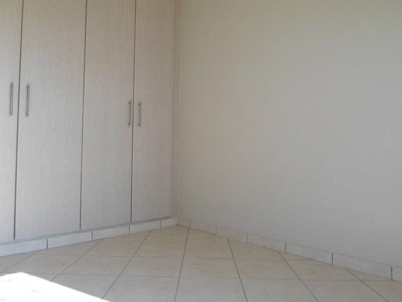 An empty bedroom corner featuring neutral tiled flooring and built-in wooden cupboards.