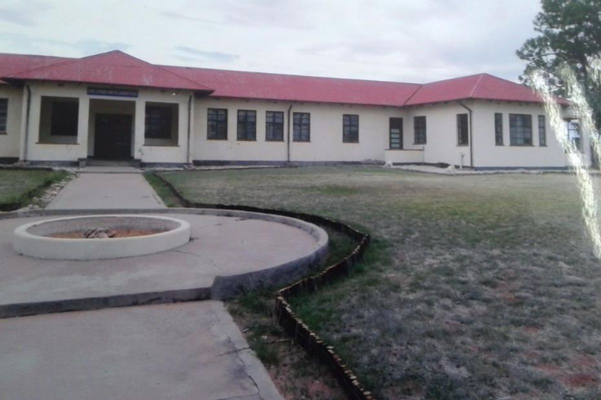 A view of the rear exterior of the property featuring a large building with a red roof, concrete walkway, and a circular fire pit area.