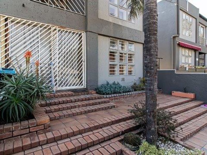 A rear exterior view of the apartment featuring a multi-level brick paved patio area with built-in planters and secure sliding door access.