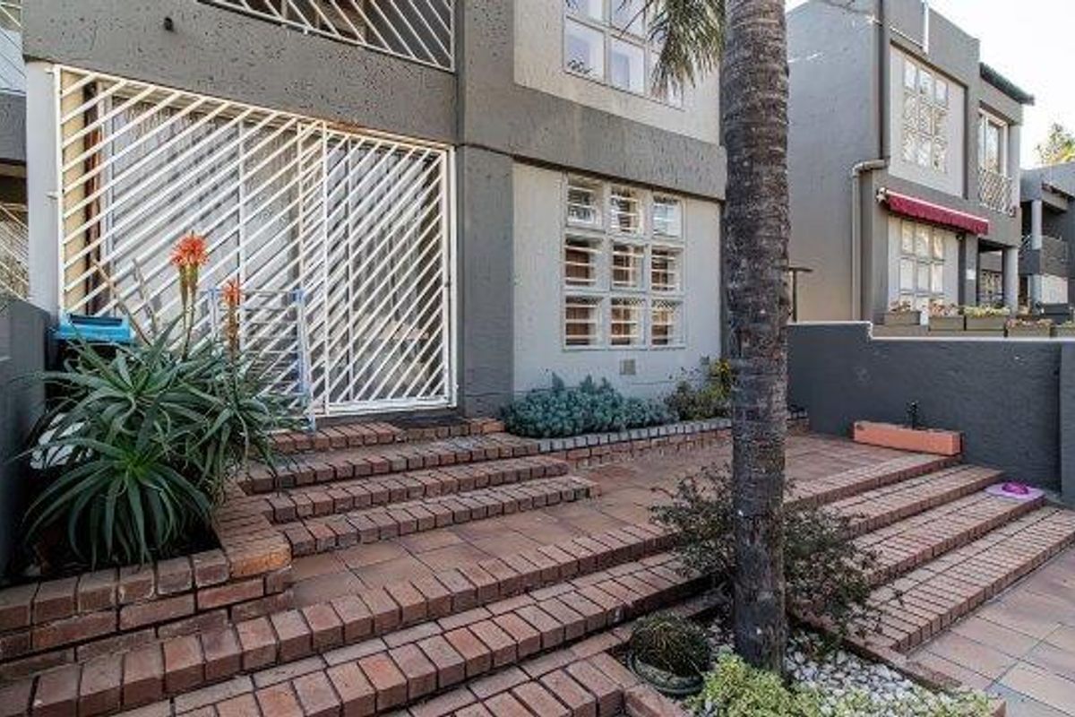 A rear exterior view of the apartment featuring a multi-level brick paved patio area with built-in planters and secure sliding door access.