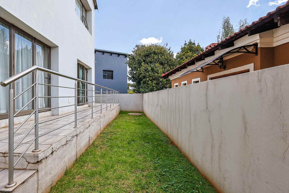 A narrow side garden area featuring a tiled patio with stainless steel railings, adjacent to the main house structure and a boundary wall.