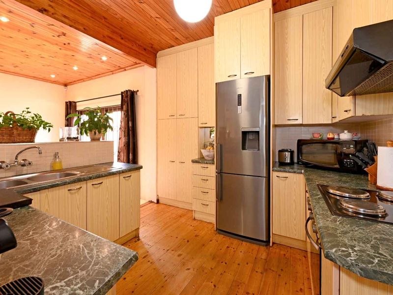 A functional kitchen featuring light wood cabinetry, stone-look laminate countertops, timber flooring, and a warm timber-paneled ceiling.