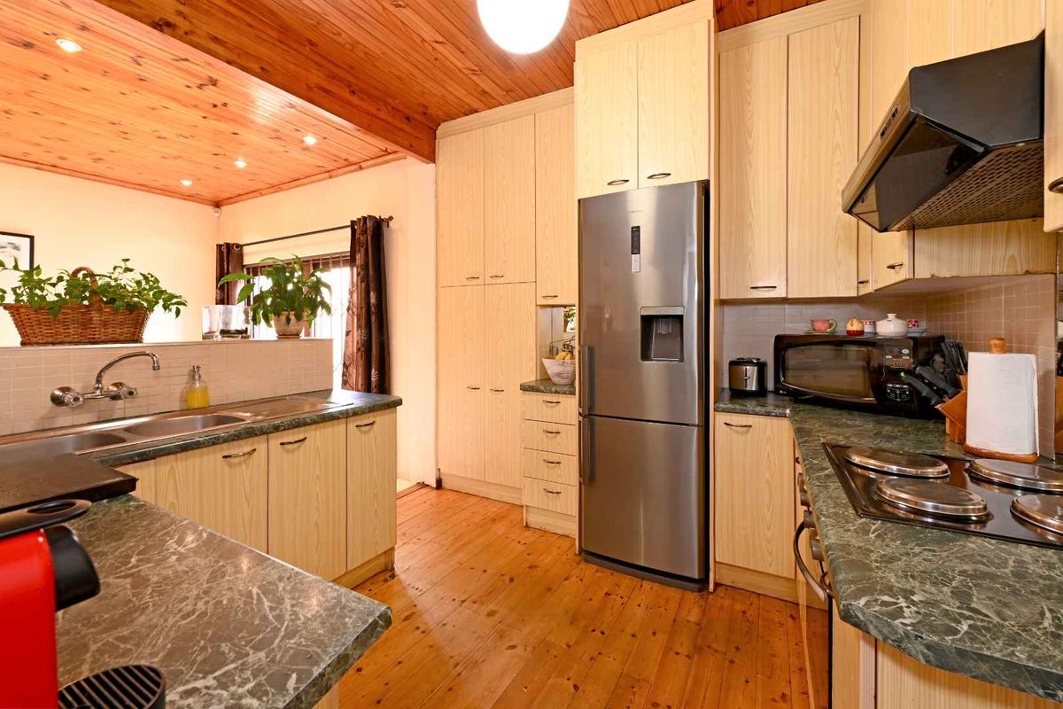 A functional kitchen featuring light wood cabinetry, stone-look laminate countertops, timber flooring, and a warm timber-paneled ceiling.