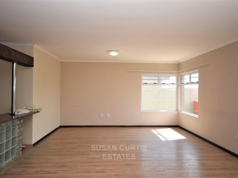 An empty living room featuring laminate flooring, a built-in breakfast bar with glass block detailing, and corner windows providing natural light.