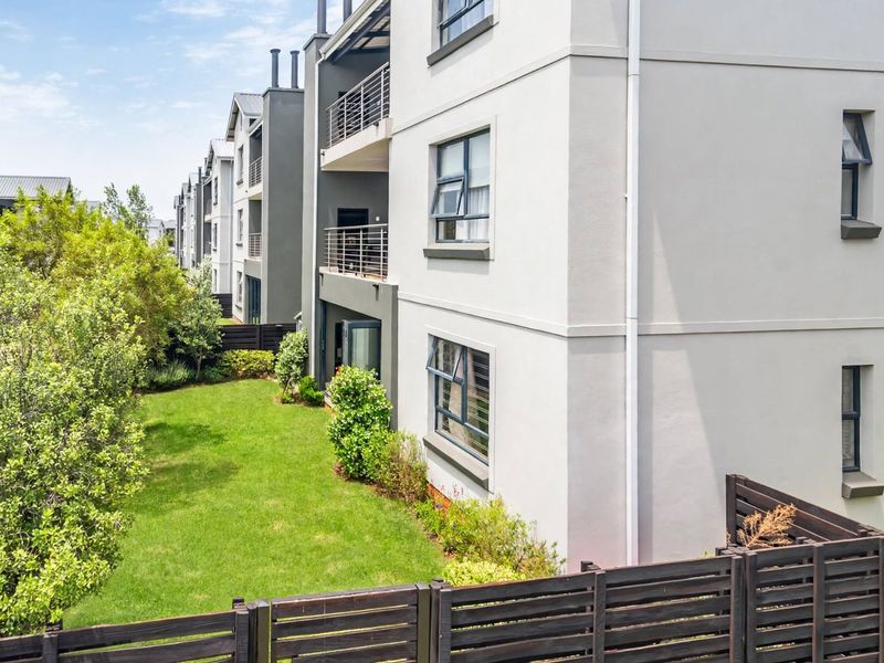 Rear view of a modern apartment complex featuring private balconies, well-maintained lawn, and timber boundary fencing.