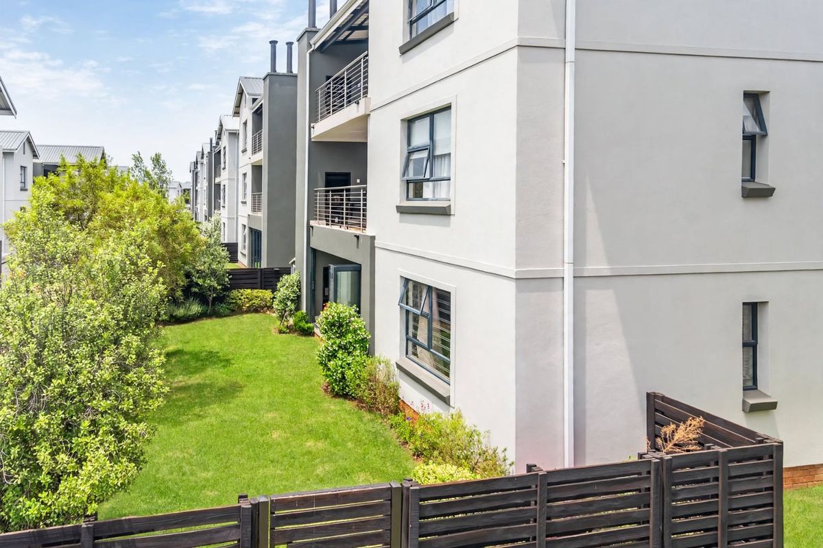 Rear view of a modern apartment complex featuring private balconies, well-maintained lawn, and timber boundary fencing.
