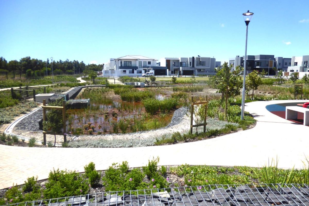 A well-maintained communal garden area featuring a landscaped pond, paved walkways, and modern street lighting within a residential estate.