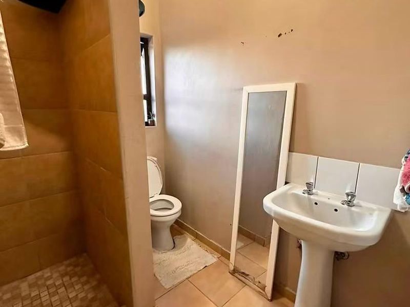 A functional bathroom featuring a pedestal basin, toilet, and a tiled shower enclosure with ceramic flooring.