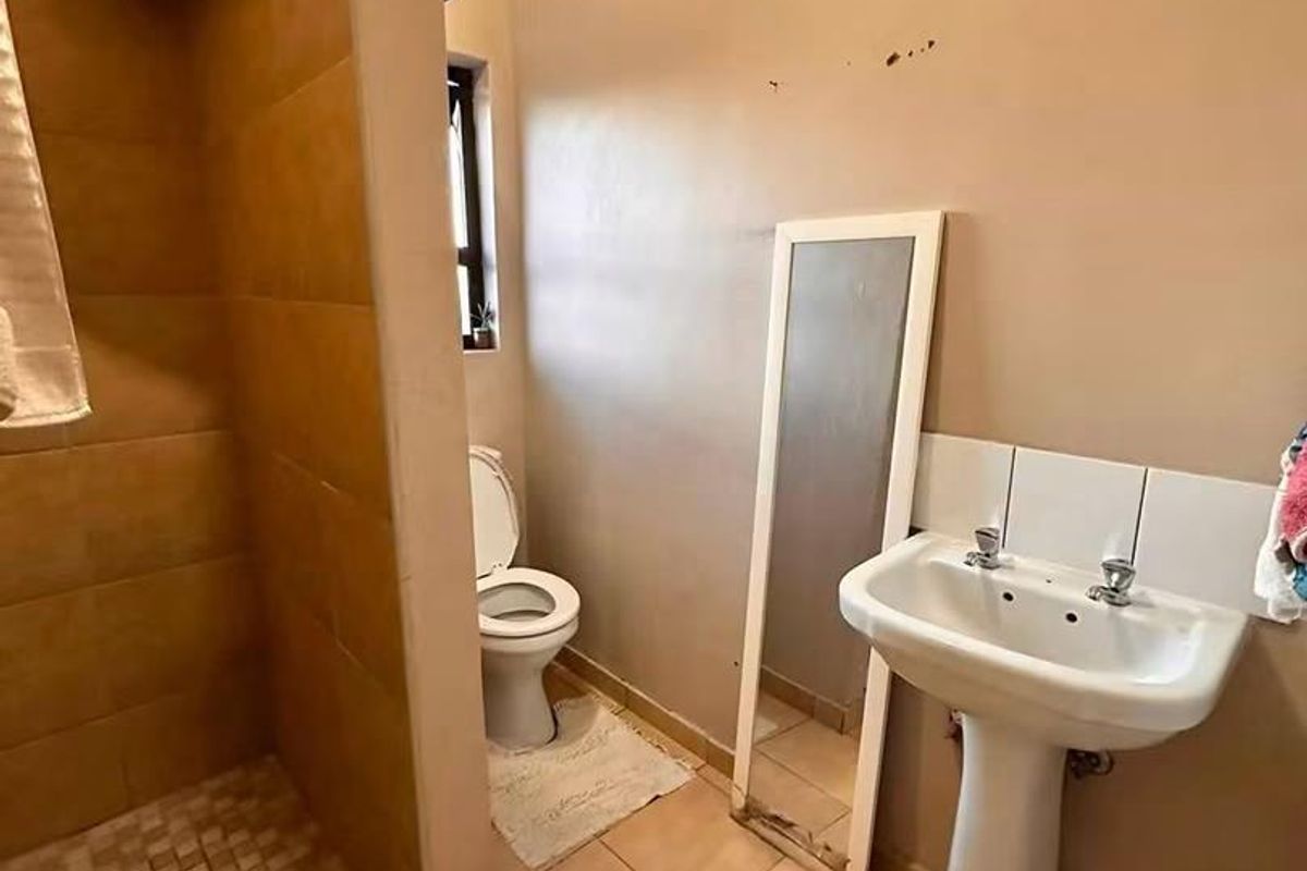 A functional bathroom featuring a pedestal basin, toilet, and a tiled shower enclosure with ceramic flooring.