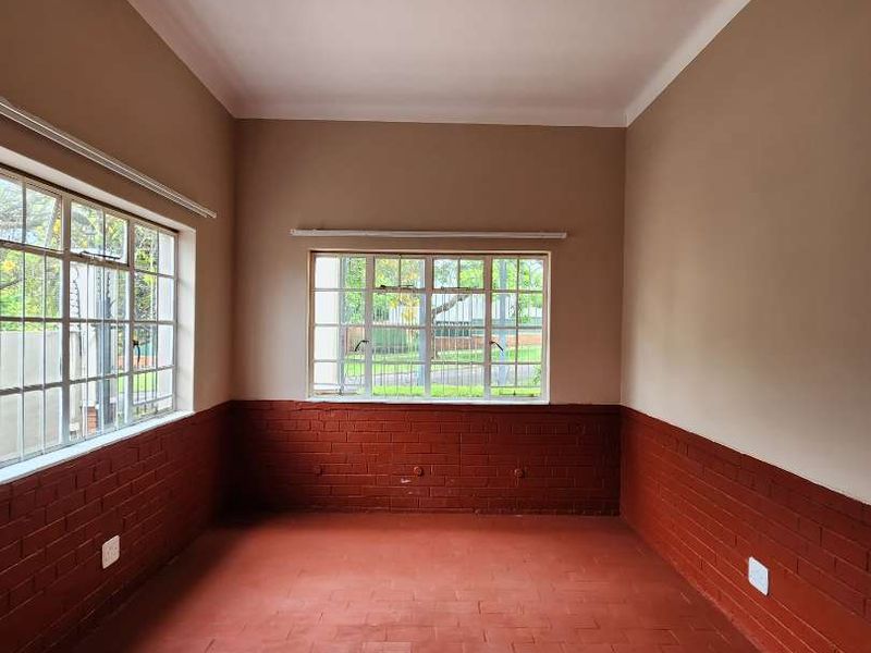 An empty living room featuring terracotta tile flooring, exposed brick lower walls, and steel frame windows, offering a blank canvas for renovation.