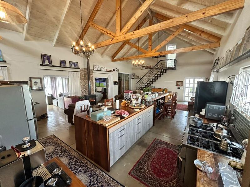 Spacious open-plan living area featuring a vaulted ceiling with exposed timber trusses, a central kitchen island, and a mezzanine level with a staircase.