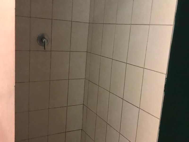 A basic shower enclosure featuring tiled walls and floor, equipped with a standard shower head and mixer tap.