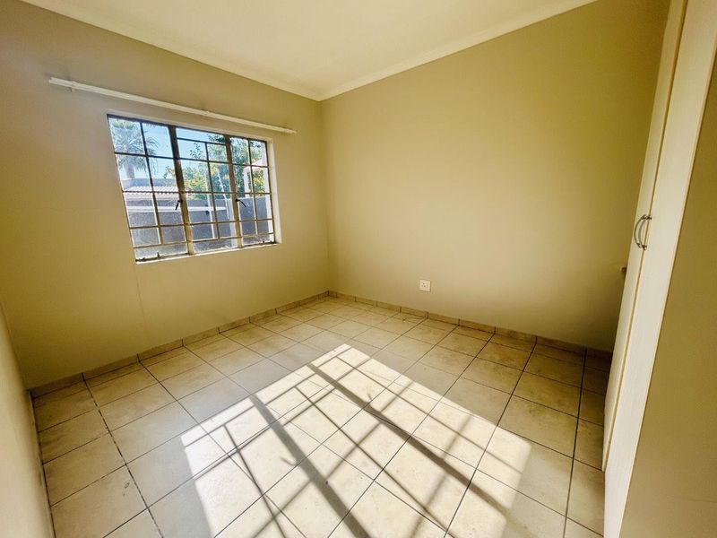A vacant bedroom featuring neutral wall paint, tiled flooring, and a built-in cupboard with natural light entering through a window with security bars.