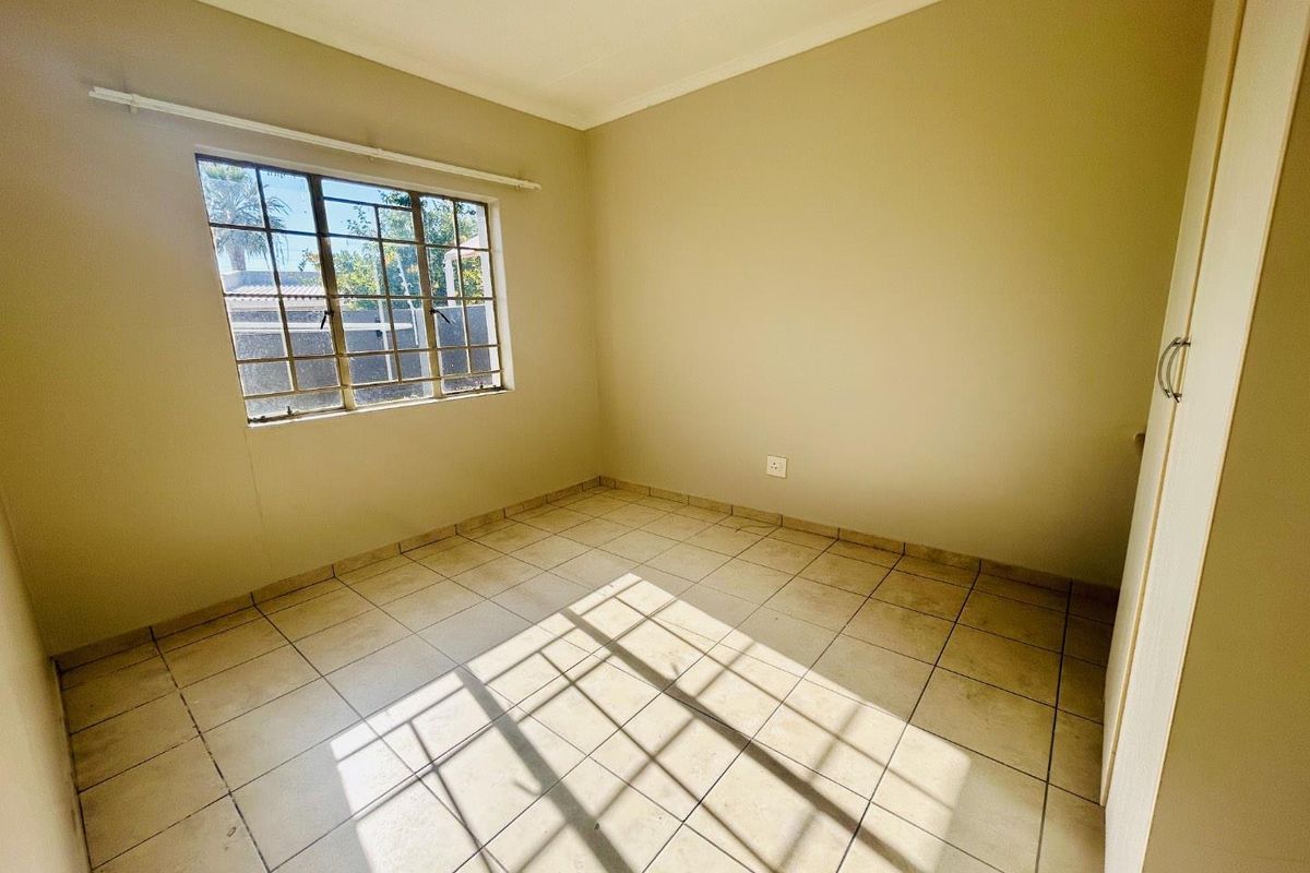 A vacant bedroom featuring neutral wall paint, tiled flooring, and a built-in cupboard with natural light entering through a window with security bars.