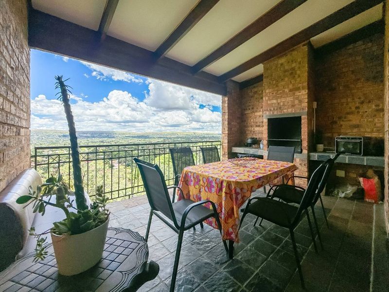 Covered patio featuring a built-in braai, exposed timber ceiling beams, and slate flooring, offering expansive elevated views over the surrounding landscape.