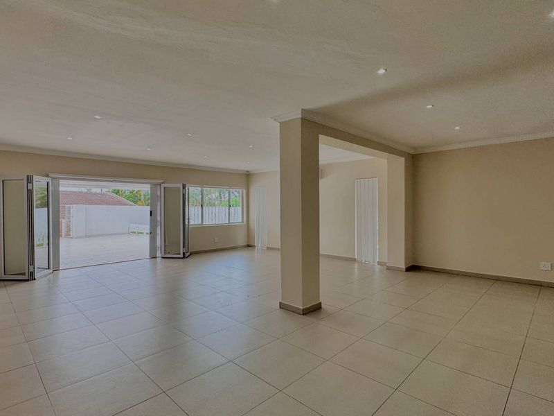 Spacious, light-filled open-plan living area featuring neutral tiled flooring, recessed downlights, and bi-fold doors providing seamless access to the outdoor patio.