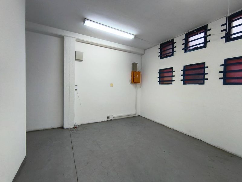A clean, empty utility space featuring concrete flooring, secure window bars, and an accessible electrical distribution board, suitable for storage or workshop use.