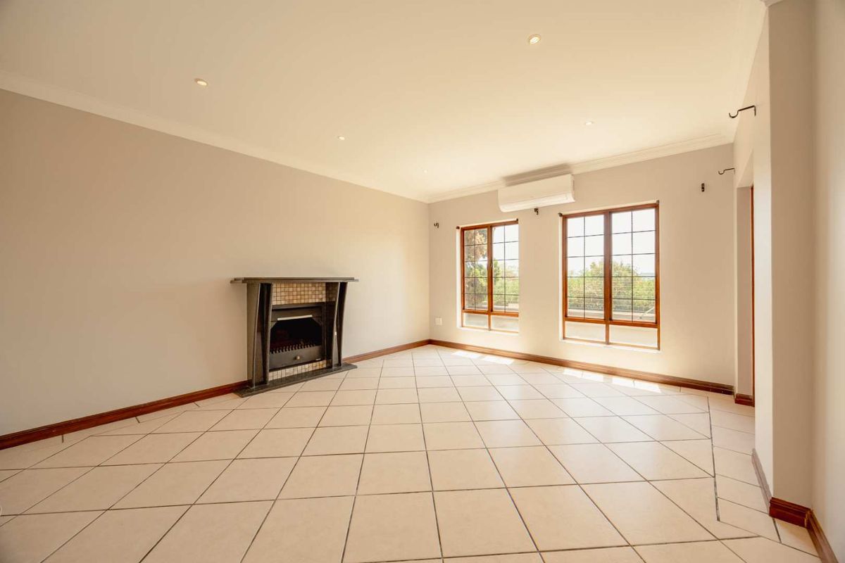 Spacious, light-filled living room featuring tiled flooring, a built-in fireplace, and an air conditioning unit, offering a clean and versatile space.