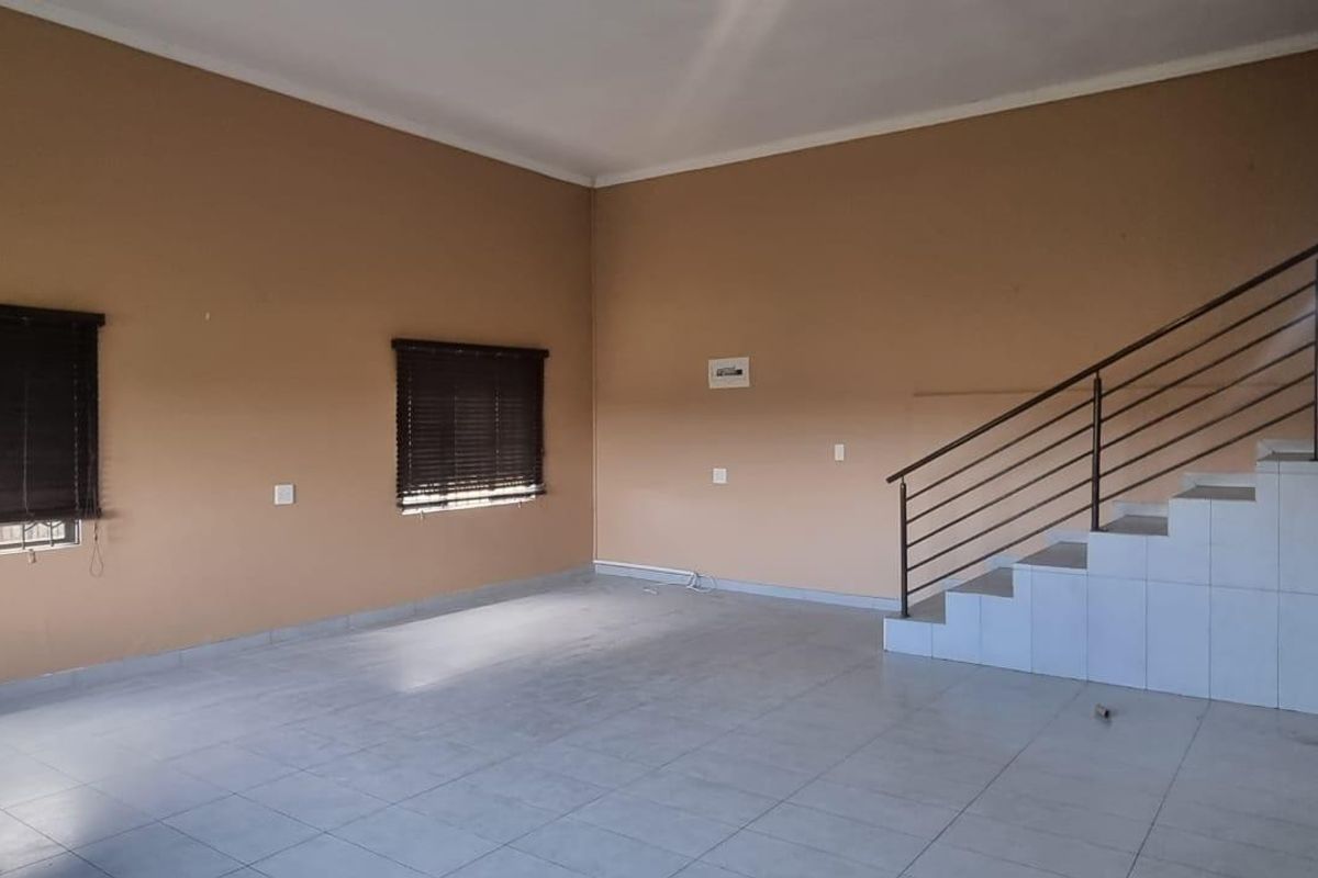 An empty, open-plan living area featuring neutral-toned walls, tiled flooring, and a staircase with a modern metal railing.