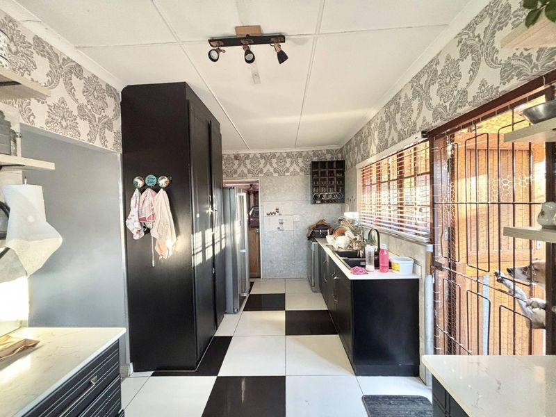 A functional kitchen featuring black cabinetry, contrasting checkerboard floor tiles, and ample counter space with a double sink and integrated lighting.