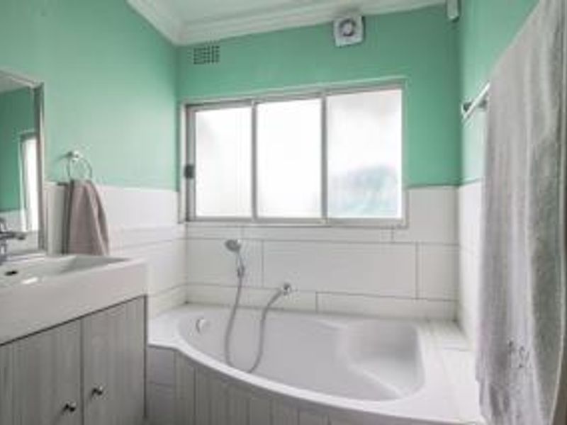 A functional bathroom featuring a built-in vanity with basin, a bathtub with shower mixer, and tiled splashbacks.